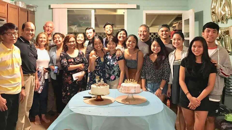 A group of people standing around a table with two cakes on it.
